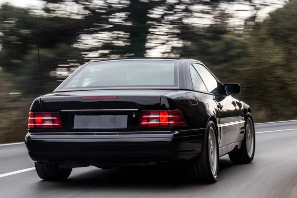 Black sedan car high speed drive on the road of the forest, red lights on — Stock Photo, Image