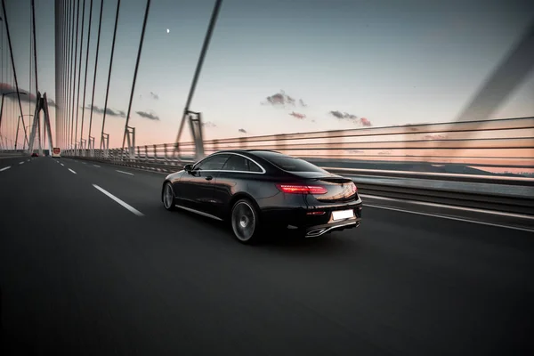 Güneşli bir havada köprüden geçen klasik siyah bir sedan araba.