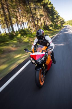 Turuncu renkli motosiklet ve kasklı bir sürücü.