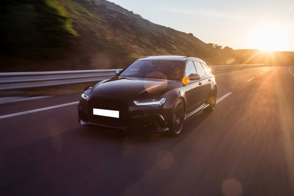 Svart bil kjører i solnedgangen på motorveien. – stockfoto
