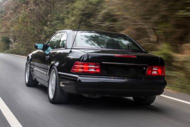 Yeşil ormanda giden siyah bir sedan.