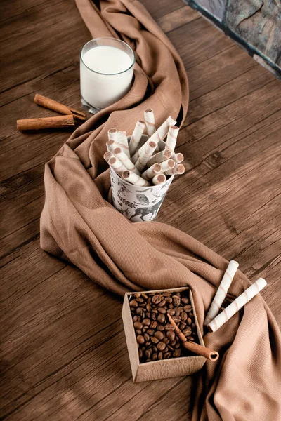 Kaffebönor, våffelpinnar och ett glas mjölk insvept i en halsduk. ovanifrån — Stockfoto