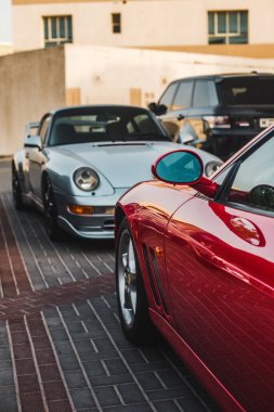 Bahçeye park etmiş gümüş ve kırmızı spor sedanları.