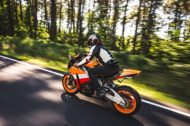 Turuncu renkli motosiklet, kasklı ve teçhizatlı bir sürücü.