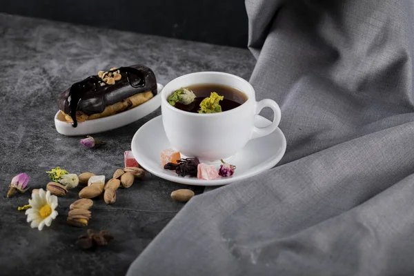 Чашка чая с шоколадным эклером и фисташками — стоковое фото