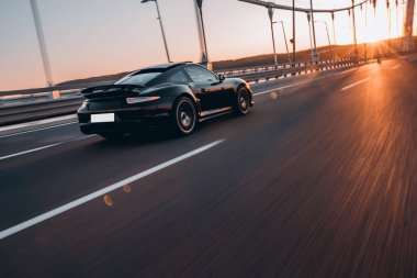 Siyah spor sedan gün batımında sürüyor.