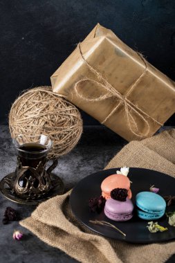 Siyah bir tabakta renkli makaronlar ve bir bardak çay kırsal bir zeminde hediye kutularıyla.