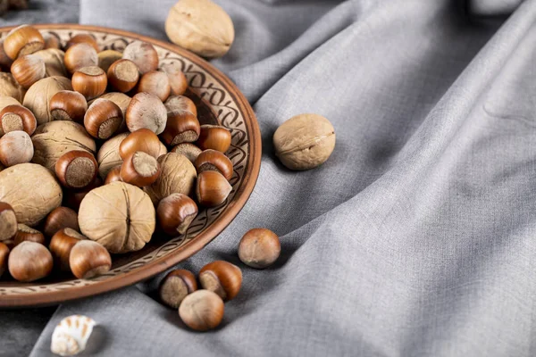 Gemengde noten in een decoratieve aardewerk plaat geïsoleerd op blauw tafelkleed — Stockfoto