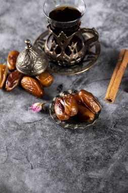 Bir bardak çay ve tarçın çubuklarıyla etnik stil bir tabakta doğulu hurmalar.