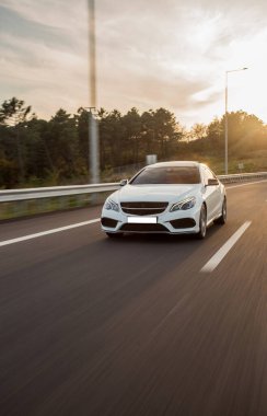 Beyaz birinci sınıf araba gün batımında yeşil tarlaları geçiyor.