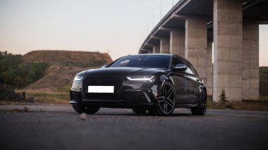 Köprünün altına park etmiş siyah bir off-road aracı, ön ışıklar açık.