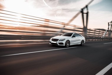 Beyaz birinci sınıf bir sedan araba. Köprüde, güneşin altında gidiyor.