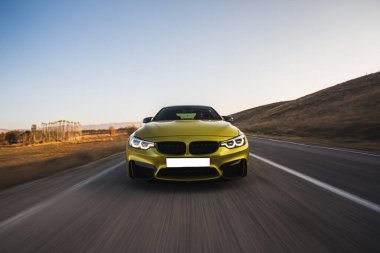 Yeşil lüks sedan araba tepeleri aşarak otoyolda yüksek hızda gidiyor.