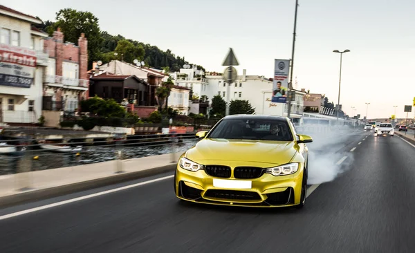 Żółta marka samochód sportowy jazdy przed budynkiem z dużą prędkością — Zdjęcie stockowe
