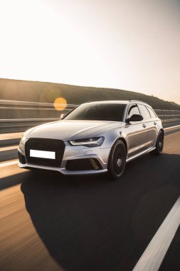 Gümüş renkli hatchback gün batımında yolda gidiyor.