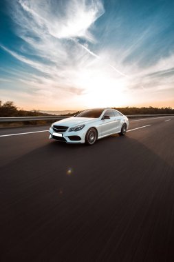 Mavi gökyüzünün altında beyaz lüks bir sedan araba sürüyordu.