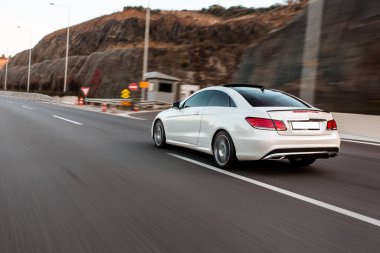 Yeşil tepeler boyunca otoyolda giden beyaz birinci sınıf bir sedan araba.