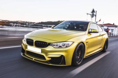 Dağlarla çevrili bir sahil limanının yolunda spor model sarı bir sedan sürüyordu.