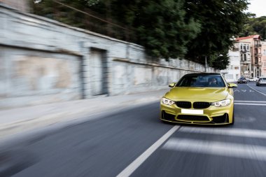 Alacakaranlıkta yeşil bölgelerden geçen şehir yolunda sarı spor araba sürüyorum.