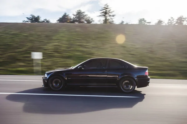 Schwarzer Luxus-Sportwagen mit roter Ampel fährt mit hoher Geschwindigkeit über grüne Hügel — Stockfoto