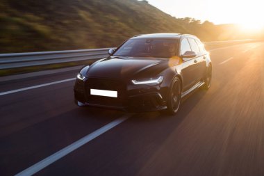 Günbatımında siyah bir sedan kullanıyor.