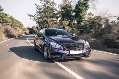 Gündüz vakti orman yolunda siyah lüks bir sedan.