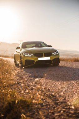 Yolda kırmızı ksenon ışıkları olan yeşil sedan araba, güneş ışığı altında ön manzara.