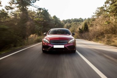 Kırmızı spor sedan, orman yolunda beyaz ksenon ışıkları, ön manzara.