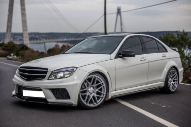 Ormanın park yerinde ksenon ışıkları, alacakaranlıkta tekerlekler ve ışıklar olan beyaz bir süvari.