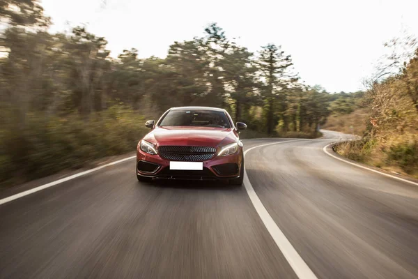 Berline sport rouge avec feux au xénon blanc sur la route forestière, champs verts autour — Photo