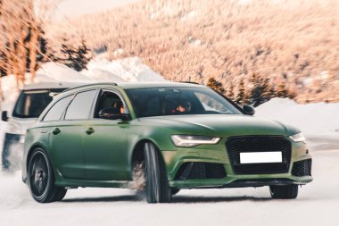 Yeşil off-road aracı karların üzerinde ormana park ediyor.