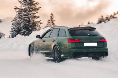 Yeşil off-road aracı, kırmızı ışıklarla ormanda gün batımında karın üstüne park ediyor.