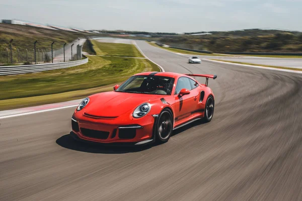 Corrida de carro esporte vermelho no traço com outros carros em campos verdes — Fotografia de Stock