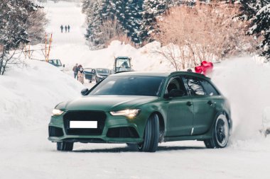 Yeşil off-road aracı, kış turizmi bölgesinde, kar üzerinde orman yolunda dalıyor.