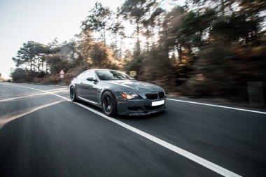 Gri birinci sınıf sedan Orman otoyolunda gün batımında