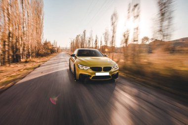 Sarı renkli hatchback ormanda otoyolda gidiyor.