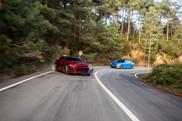 Berline sportive rouge et bleue avec feux au xénon blanc sur la route forestière le jour — Photo