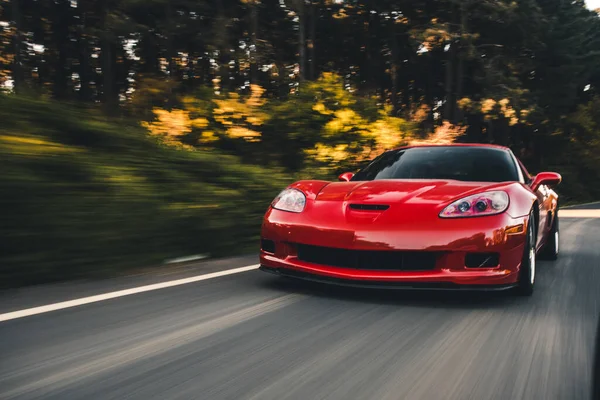 Vermelho esporte carro velocidade unidade na estrada da floresta sob a luz do sol — Fotografia de Stock