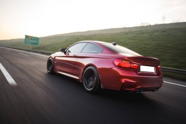 Yeşil tepelerden geçen kırmızı bir sedan taksi.