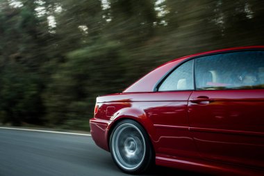 Ormanda giden kırmızı bir arabanın arka tekerleği ve kapısı.