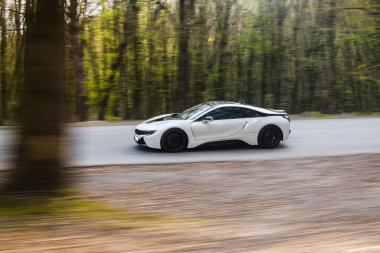 Beyaz spor model sedan taksi yeşil orman ağaçlarının arasından geçiyor.