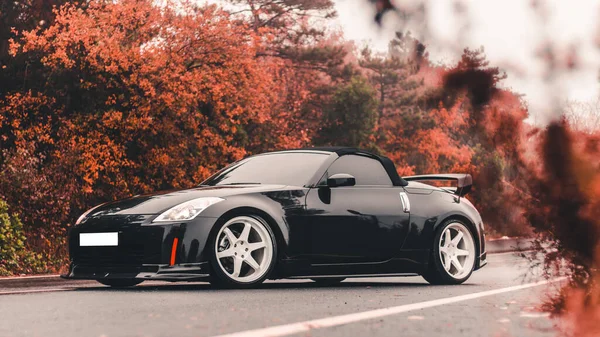 Sonbahar ormanlarında otoyola park edilmiş son model siyah spor araba. — Stok fotoğraf
