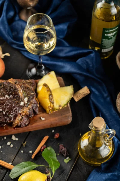 Barbacoa de carne en rodajas servida en una tabla de madera, rodajas de piña y una copa de vino blanco alrededor — Foto de Stock