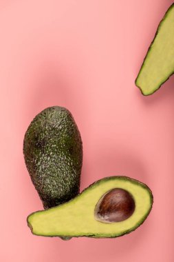 Yeşil ve yarım kesilmiş avokadolar pembe arka planda izole edilmiş.