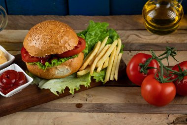 Hamburger, soğanlı rulo ve soslu kızarmış patates ve domates. 