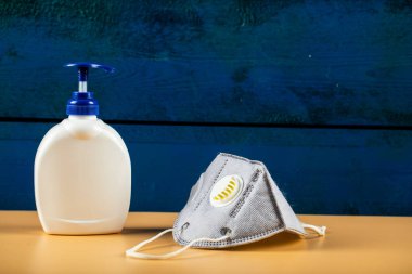 Turuncu arka planda beyaz dezenfektan kabı olan mavi modern yüz maskesi.