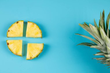 Mavi arka planda yeşil yapraklı taze ananas dilimleri