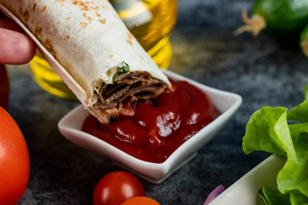 Rollo de shaurma de carne, comida árabe en la calle sumergida en ketchup en un platillo blanco —  Fotos de Stock