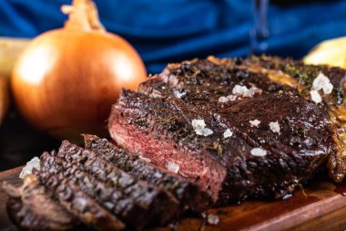 Tahtada soğanla servis edilen dilimlenmiş et barbeküsü.