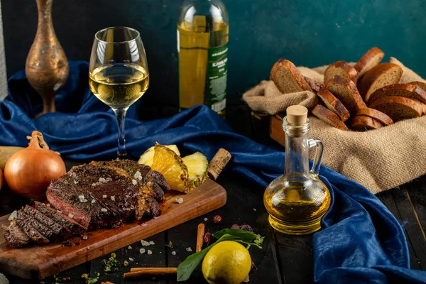 Barbacoa de carne en rodajas servida sobre tabla de madera, rodajas de piña, copa de vino, limón, aceite de oliva y bandeja de pan — Foto de Stock